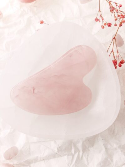 Pembe kuvars gua sha taşı çiçeklerle süslenmiş beyaz arka planda görsellenmiş